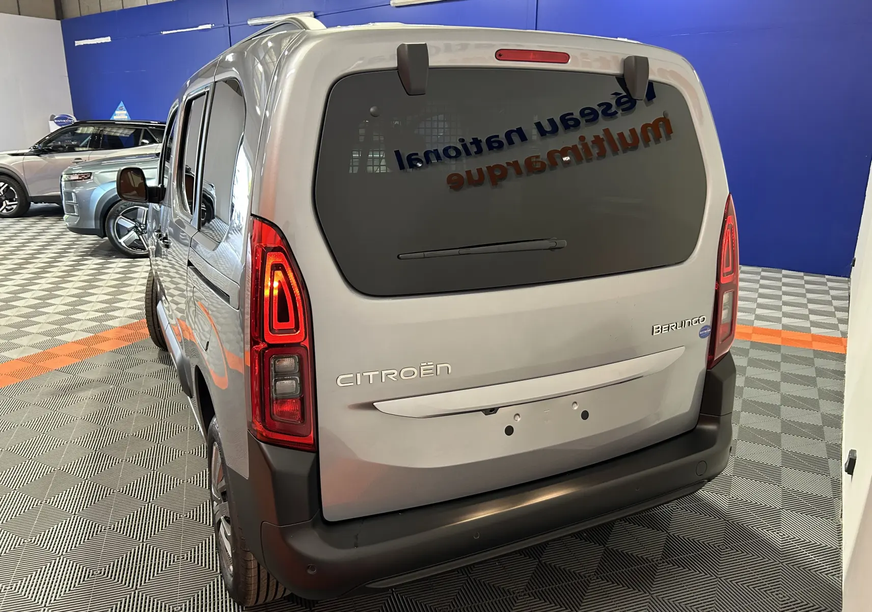 Vue 3/4 arrière droite d'un Citroën Berlingo Multispace gris acier avec vitres surteintées et feux arrière allumés.