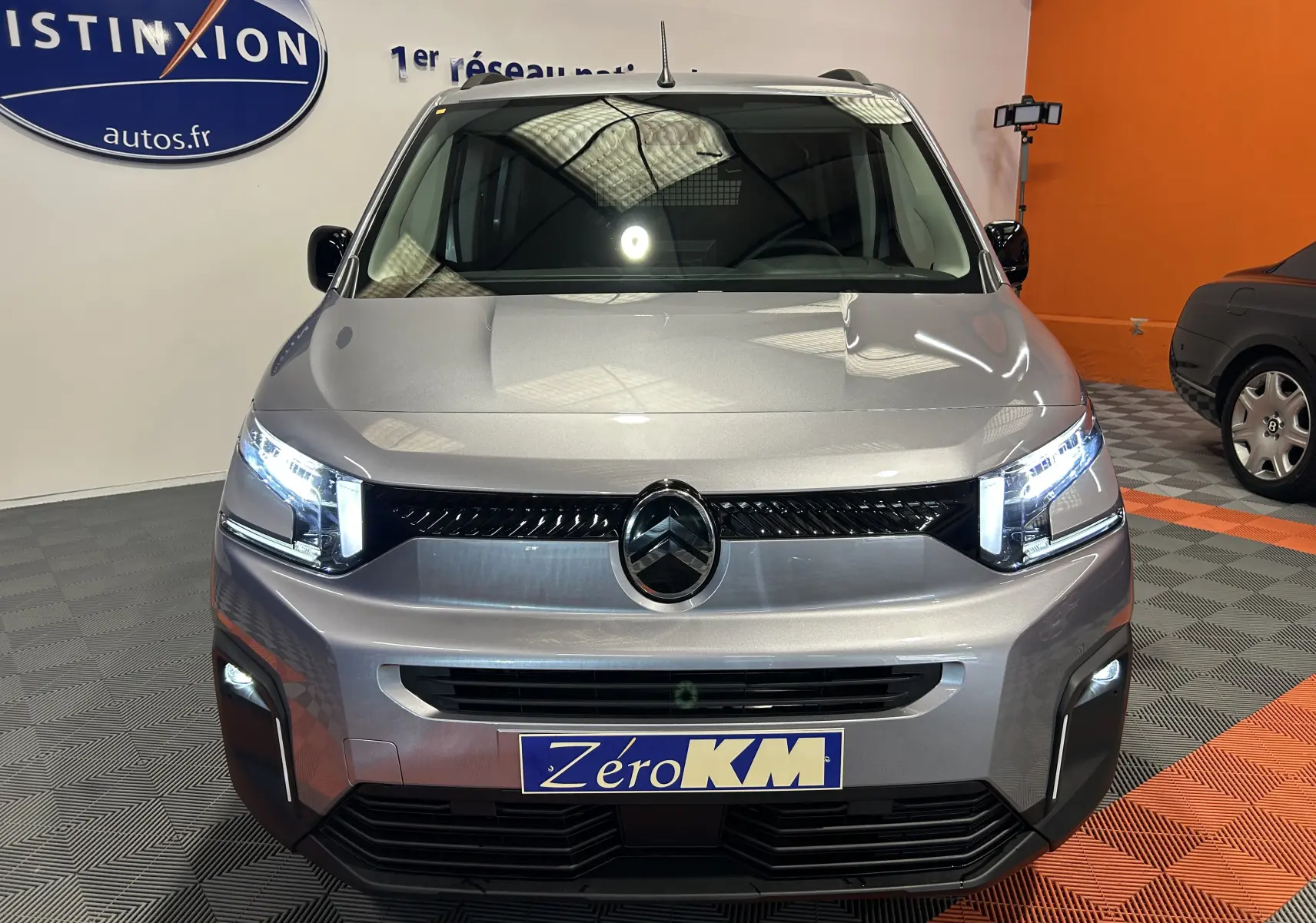 Vue frontale d'un Citroën Berlingo Multispace gris acier avec phares LED allumés en showroom.