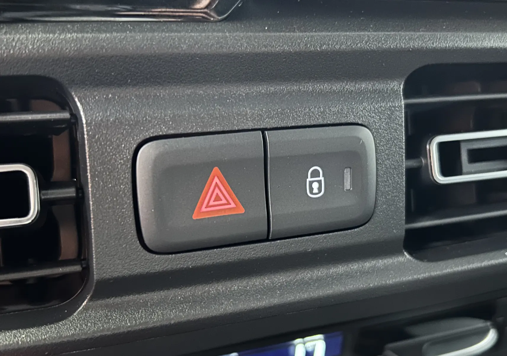 Gros plan sur les boutons d'alerte et de verrouillage centralisé du tableau de bord du Citroën Berlingo Multispace gris acier.