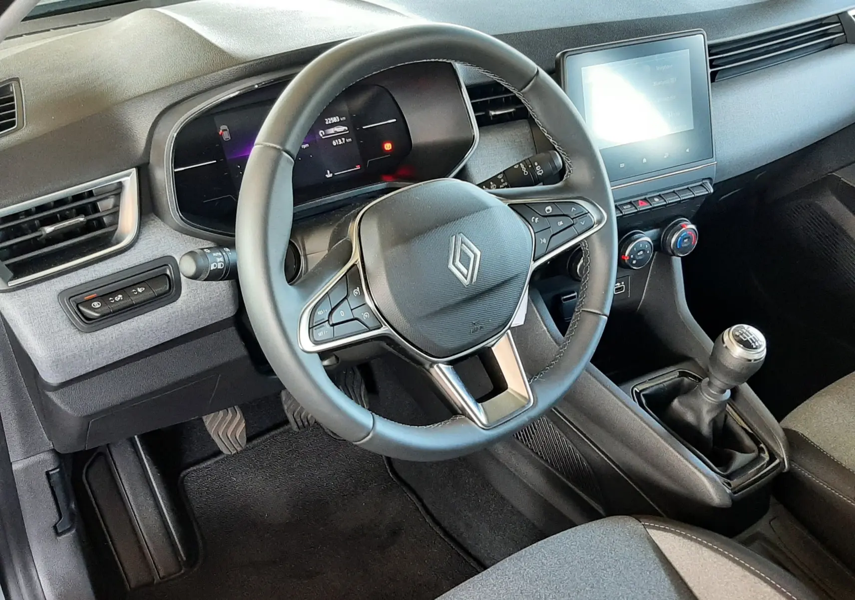 Intérieur de la Renault Clio V 1.5 Blue dCi 100ch Evolution 2024, vue côté conducteur sur le volant, tableau de bord et levier de vitesses manuel.