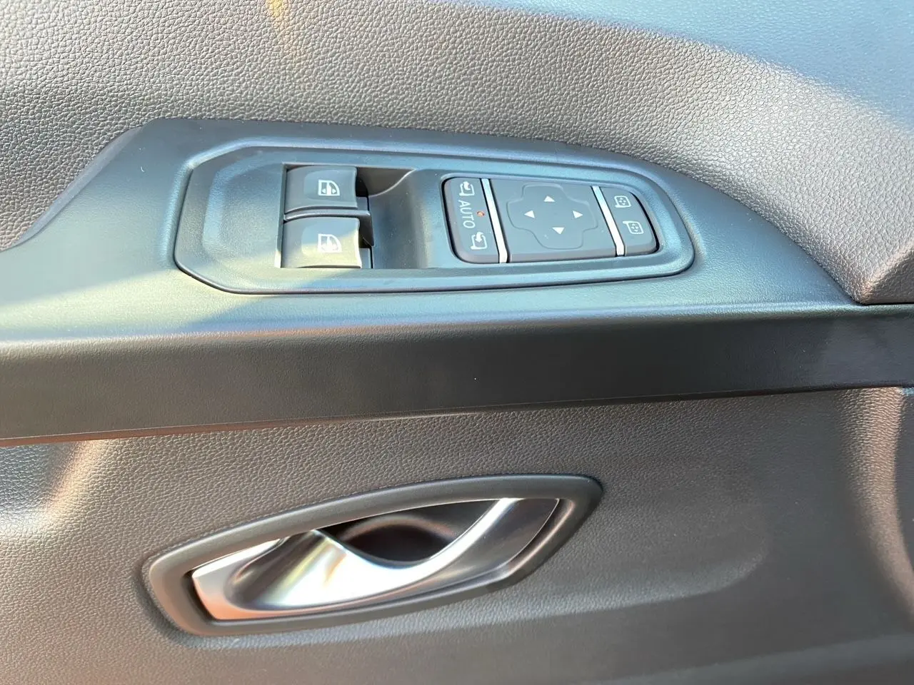 Gros plan sur la commande des vitres et la poignée intérieure côté gauche d'une porte noire du Renault Trafic Combi 2025.