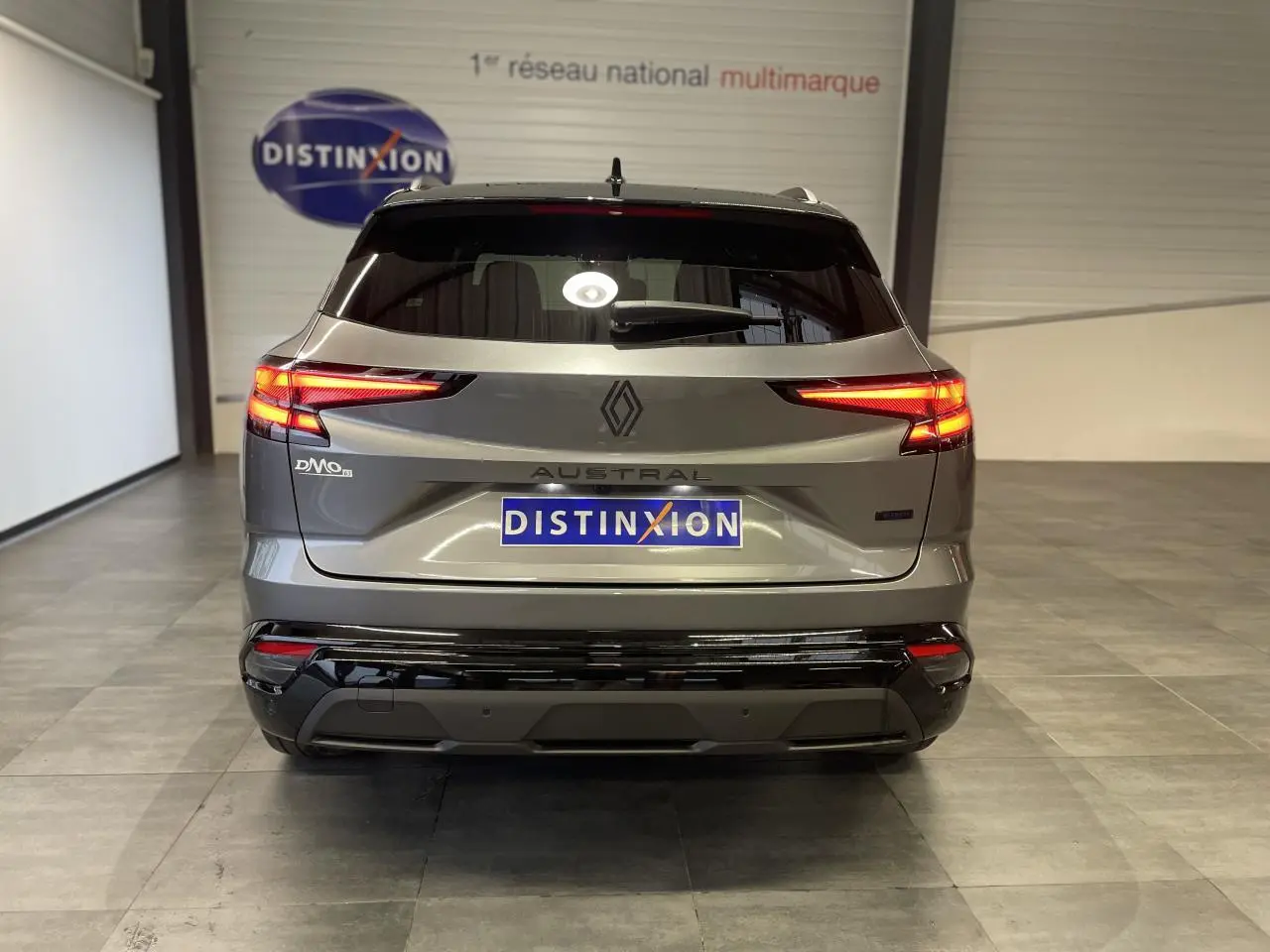 Vue arrière du Renault Austral 2025 gris Schiste métallisé avec toit noir étoilé, feux arrière allumés en intérieur showroom.