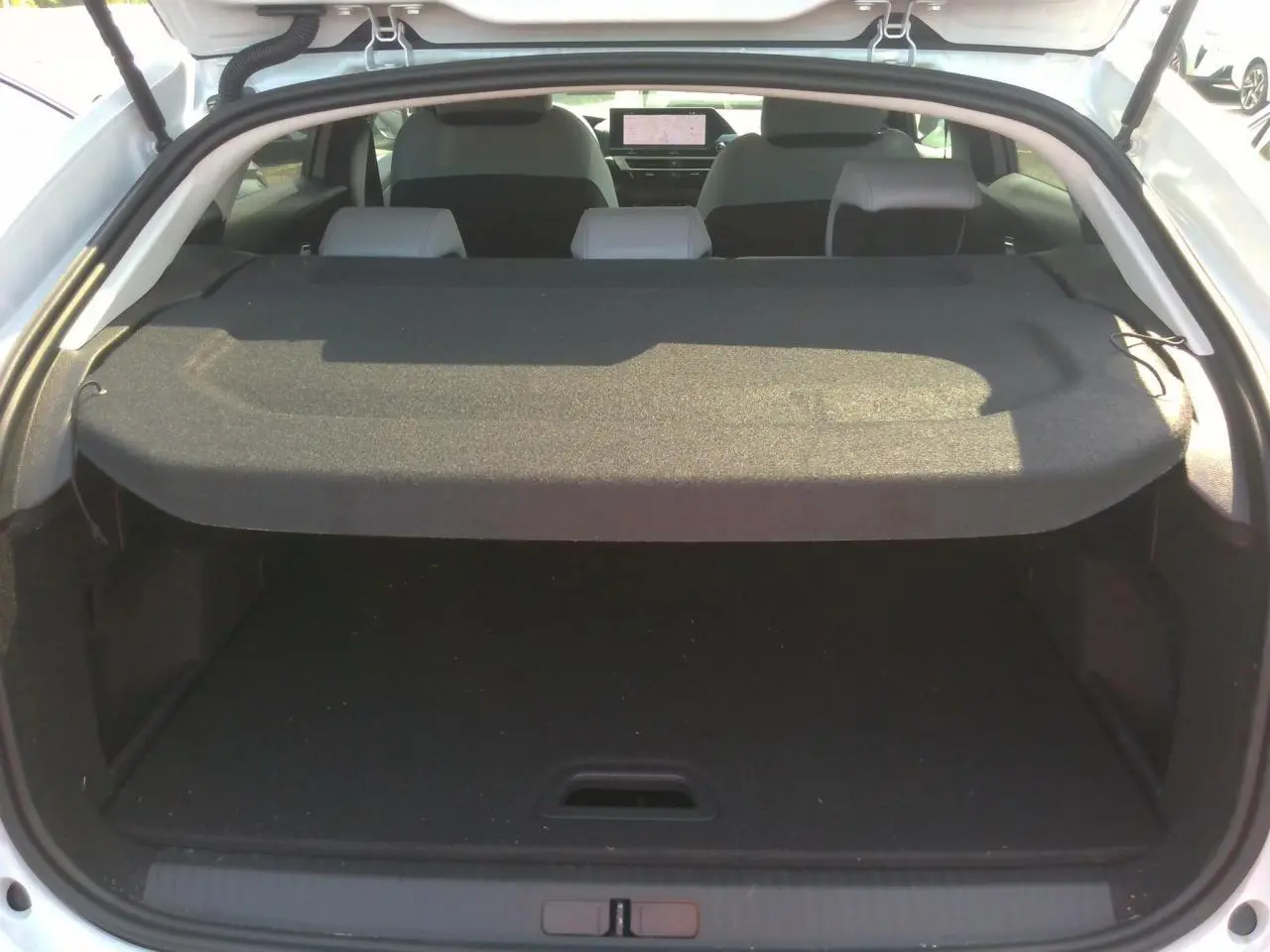 Coffre ouvert vu de l'arrière d'une Citroën C4 Hybrid 145 blanc Okénite avec tablette cache-bagages et sièges arrière visibles.