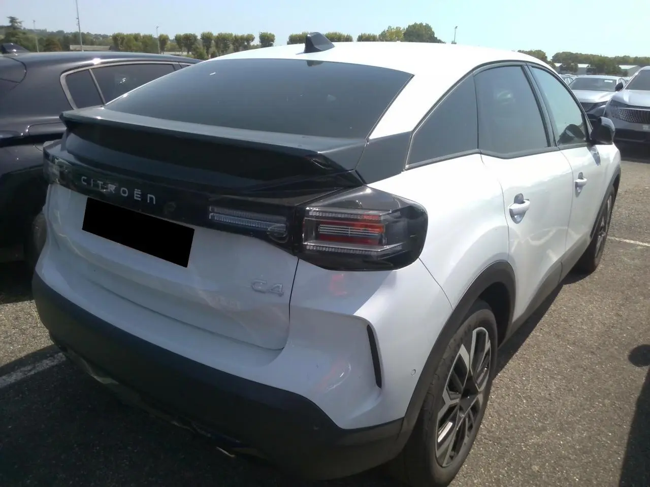 Vue 3/4 arrière droite d'une Citroën C4 blanche Okénite avec toit noir et feux arrière fumés.
