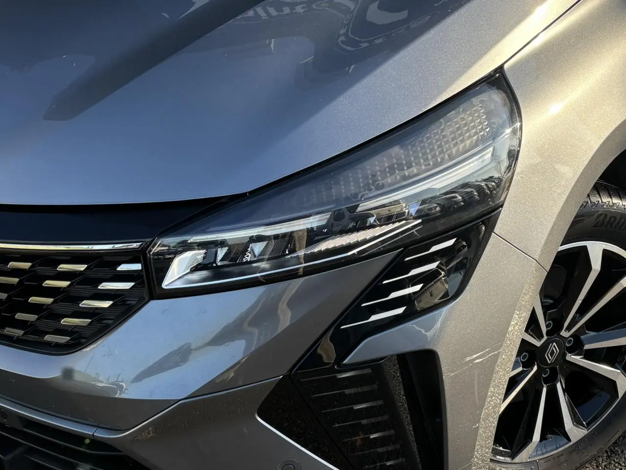 Gros plan sur l'avant droit de la Renault Clio V E-Tech Gris Schiste, mettant en valeur son phare LED et jante alliage noire.