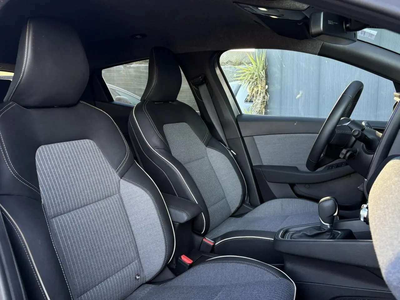 Vue intérieure côté droit de la Renault Clio 2025, sièges bi-matière gris et noir avec surpiqûres blanches.