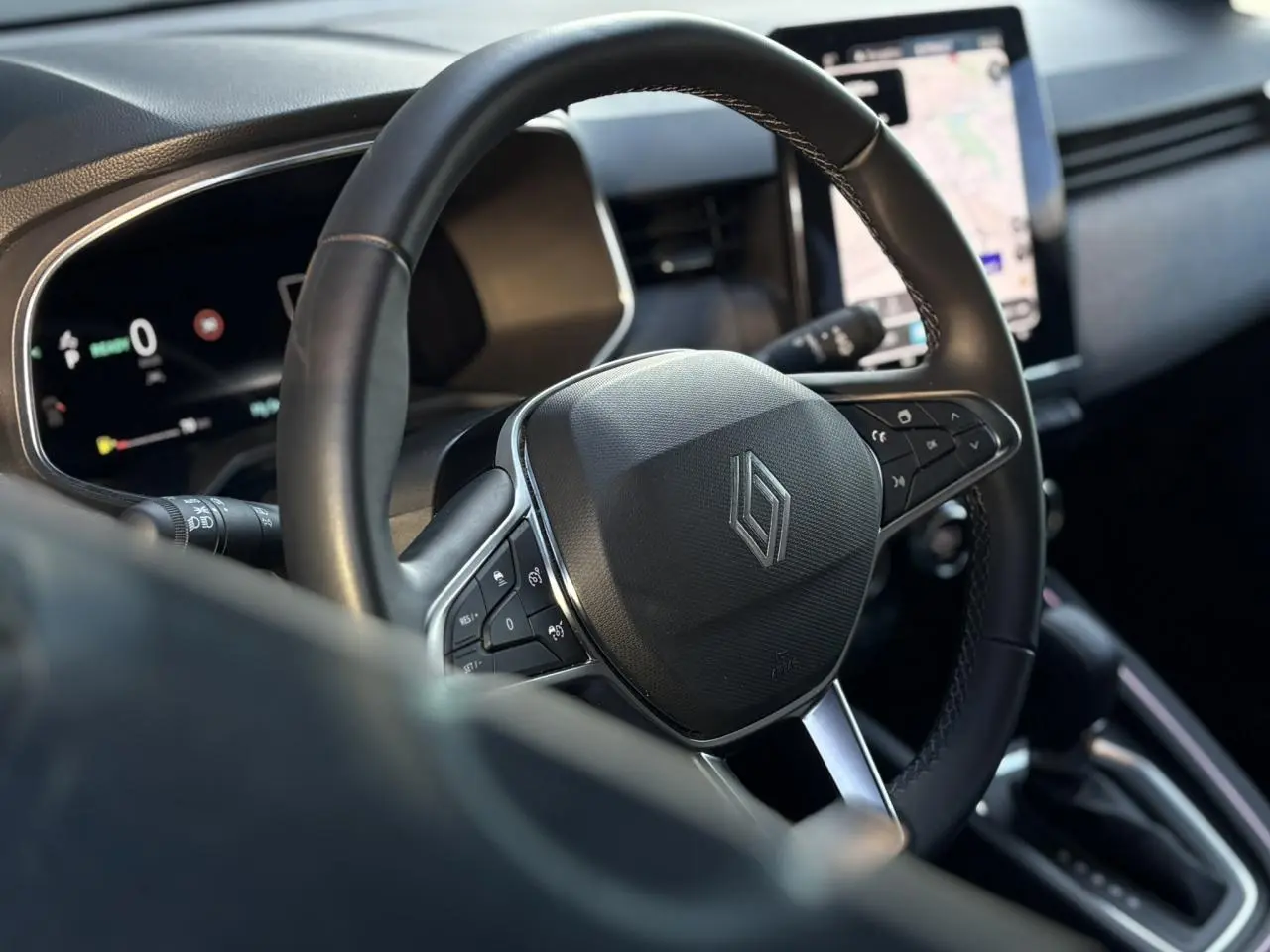 Gros plan sur le volant multifonction noir de la Renault Clio V E-Tech avec tableau de bord numérique et écran tactile en arrière-plan.