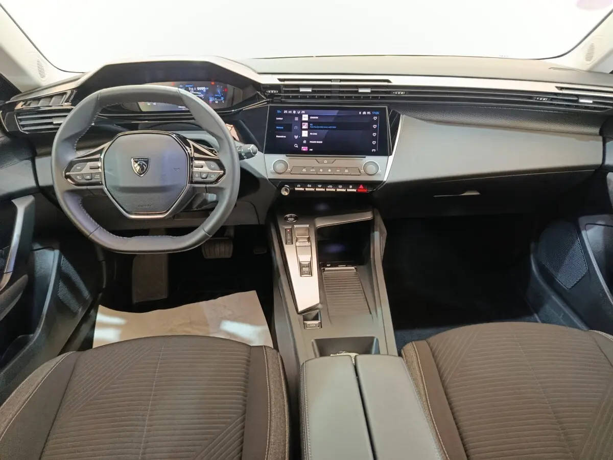 Vue intérieure avant centrée du tableau de bord et volant cuir noir de la Peugeot 308 2022 PureTech blanche.