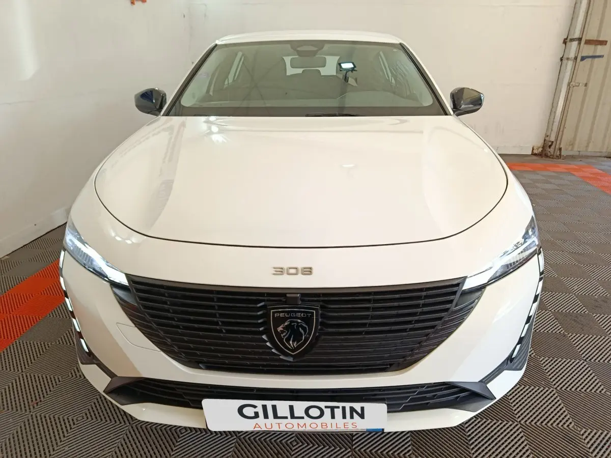 Vue frontale d'une Peugeot 308 blanche 2022 avec calandre noire et feux LED allumés en intérieur.