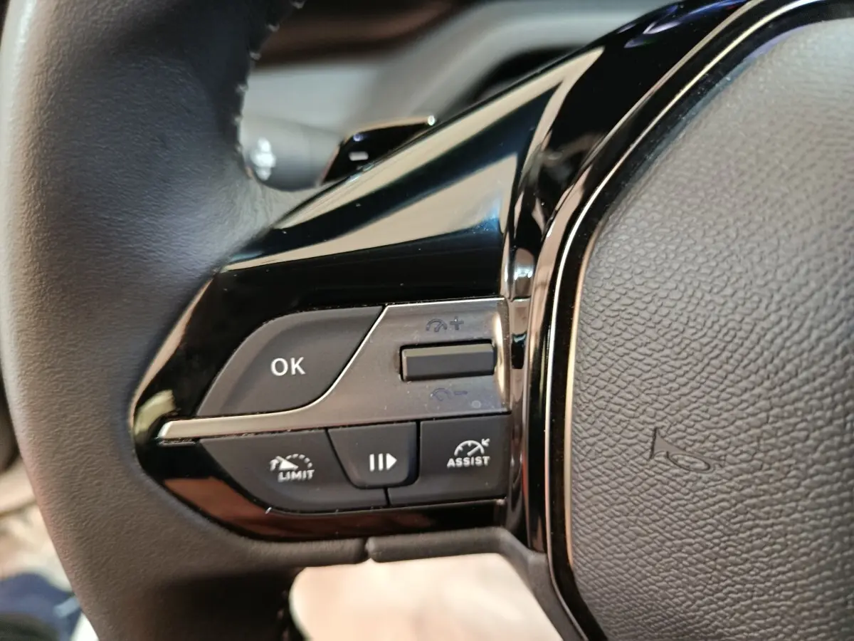 Gros plan sur les commandes multifonctions noires à gauche du volant cuir d’une Peugeot 308 blanche.