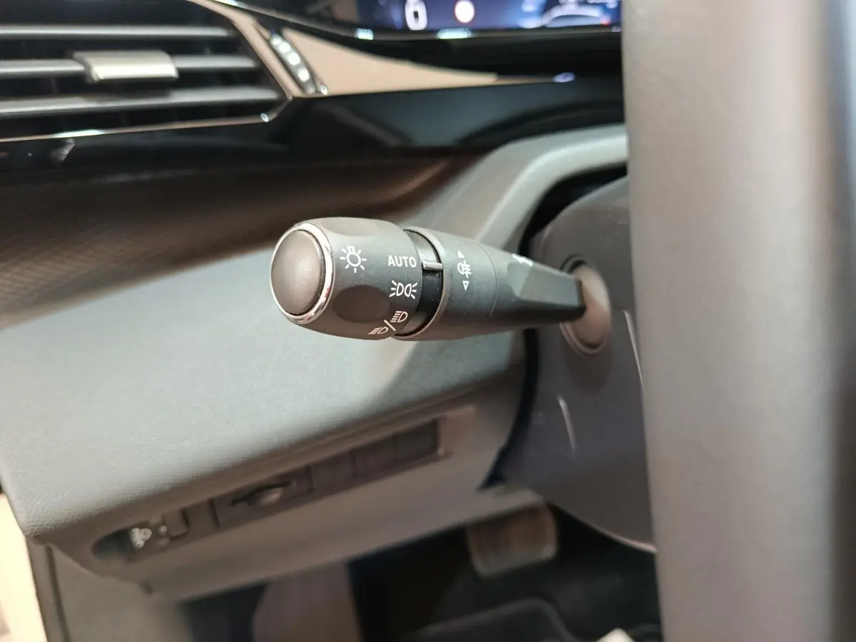 Gros plan sur la commande des feux à gauche du volant dans l’habitacle sombre d’une Peugeot 308 blanche.