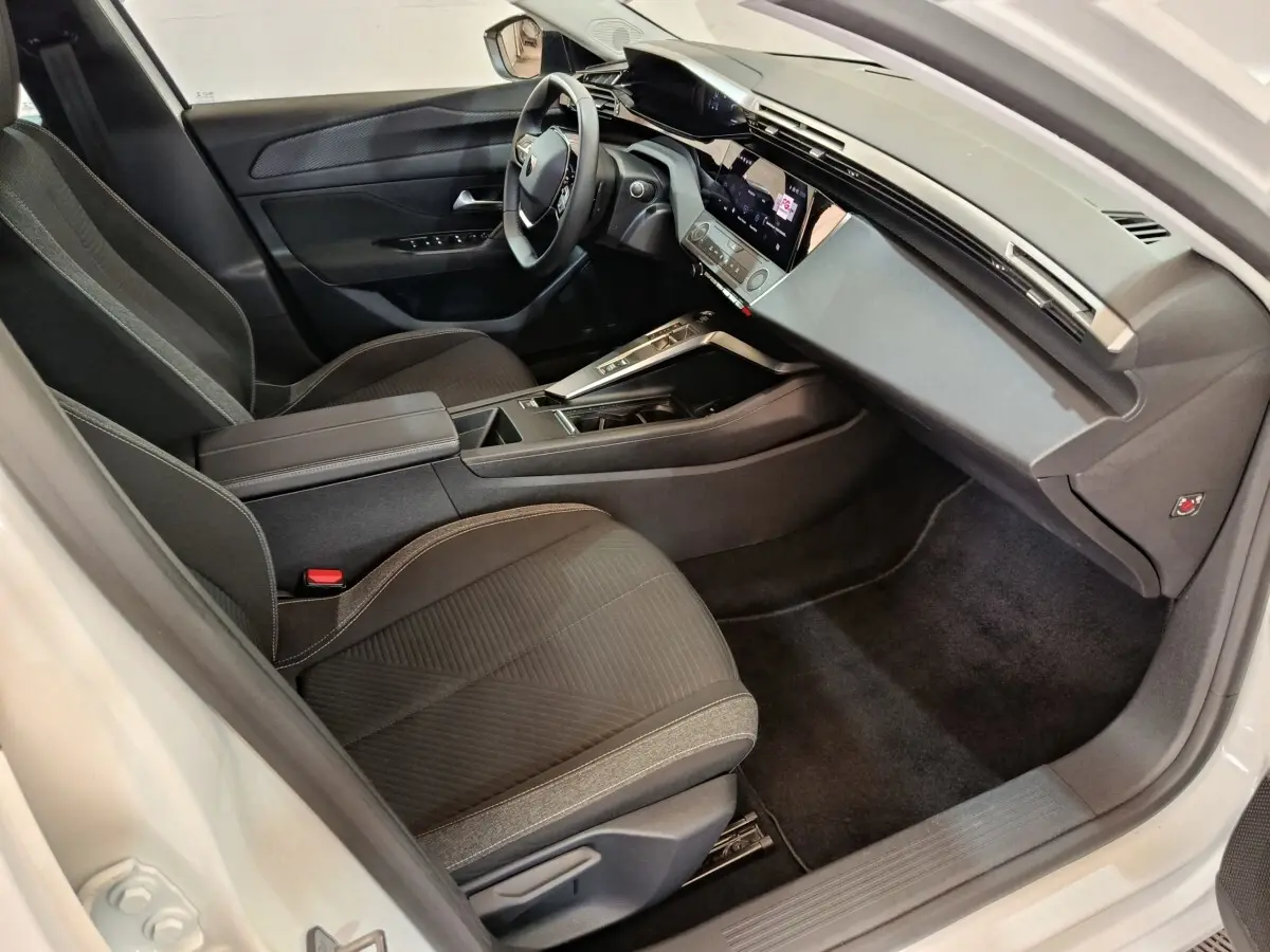Intérieur avant droit de la Peugeot 308 blanche 2022, avec tableau de bord digital et sièges tissu noirs.