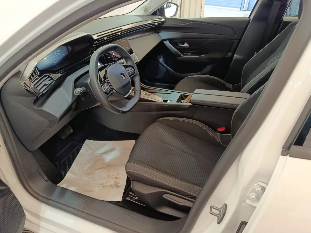 Intérieur avant droit de la Peugeot 308 blanche 2022, avec tableau de bord digital et sièges tissu noirs.