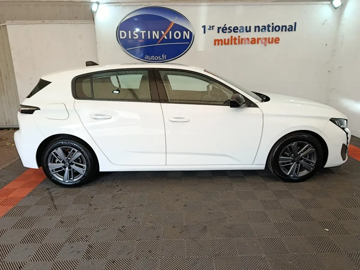 Peugeot 308 blanche vue de profil côté gauche, avec jantes alliage et rétroviseurs noirs contrastants.