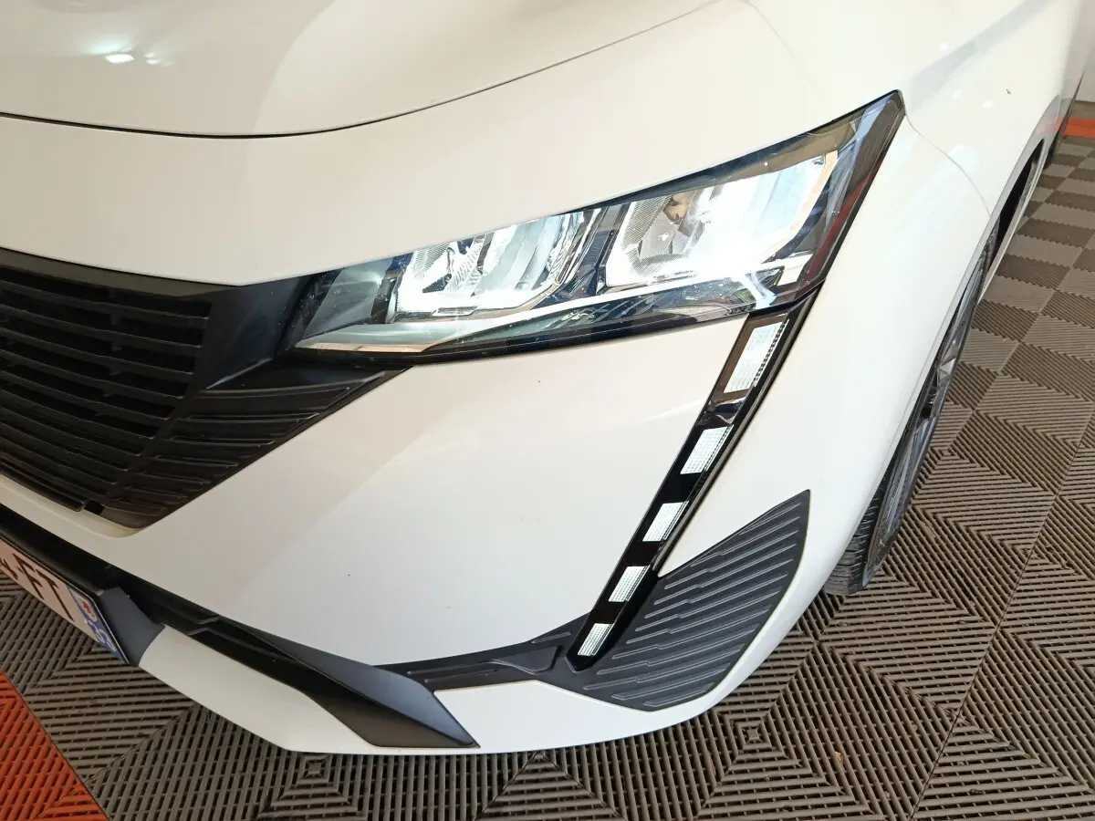 Gros plan sur l'avant droit blanc de la Peugeot 308 2022 avec phares LED et calandre noire distinctive.