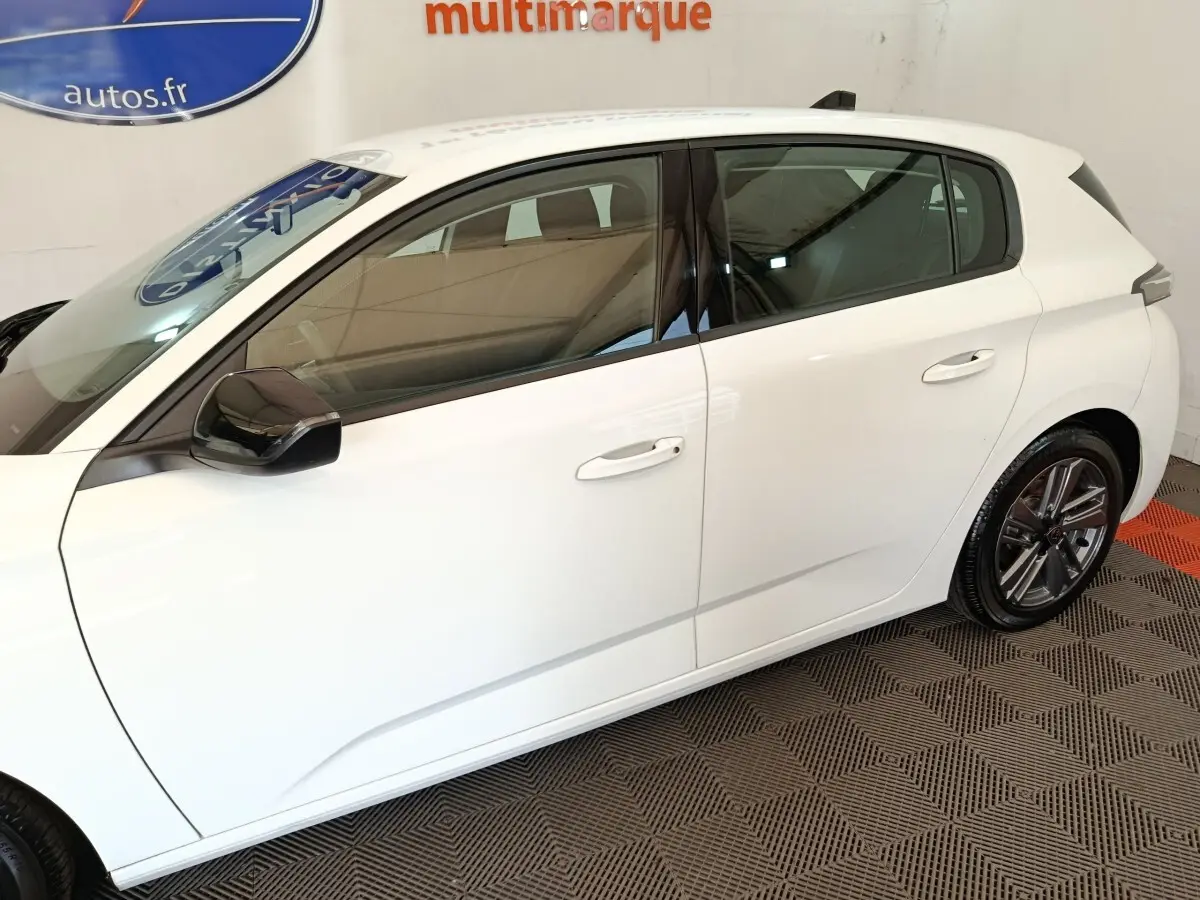 Profil droit d'une Peugeot 308 blanche 2022 avec jantes alliage et rétroviseurs noirs en intérieur showroom.