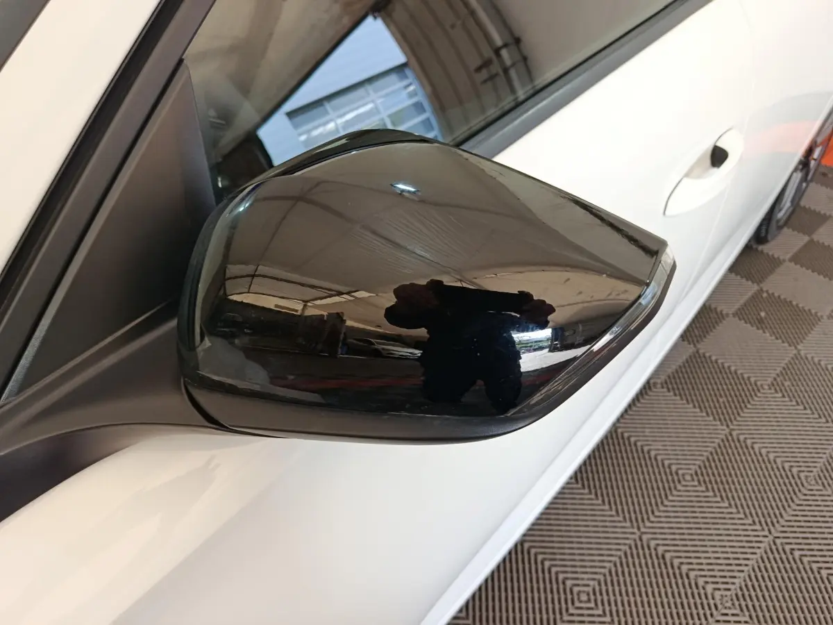 Rétroviseur noir côté conducteur d'une Peugeot 308 blanche vue de près, avec poignée de porte visible.