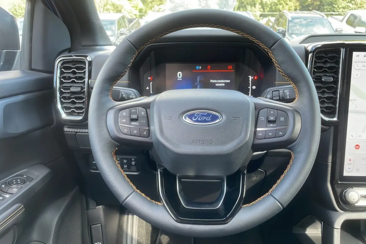 Vue rapprochée du volant cuir noir avec surpiqûres orange du Ford Ranger 2025, tableau de bord et écran tactile visibles.