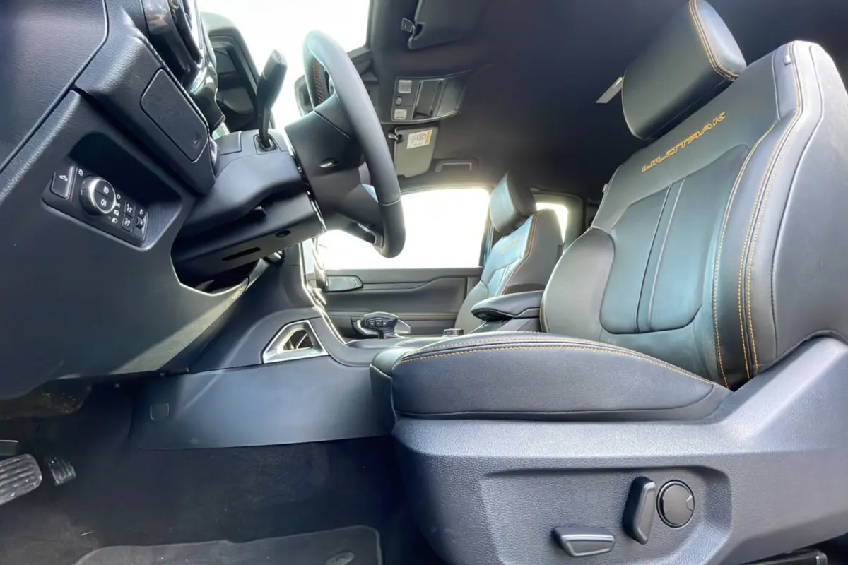 Vue intérieure côté conducteur du Ford Ranger Wildtrak 2025, sièges cuir noirs avec surpiqûres orange et logo Wildtrak brodé.
