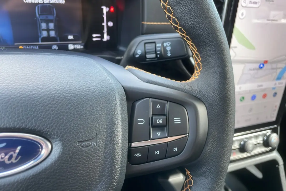 Gros plan sur le volant cuir noir avec surpiqûres orange du Ford Ranger 2025, affichage numérique et écran tactile visible.