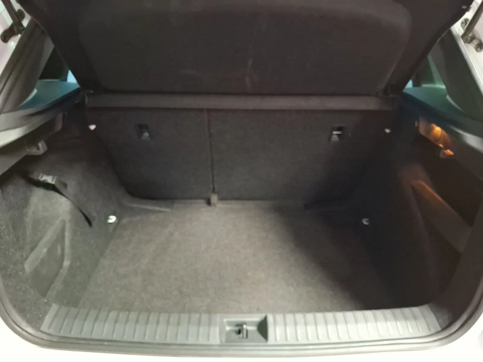 Coffre ouvert d’un Skoda Kamiq blanc, vue de l’arrière montrant l’espace de chargement vide et tapis gris.