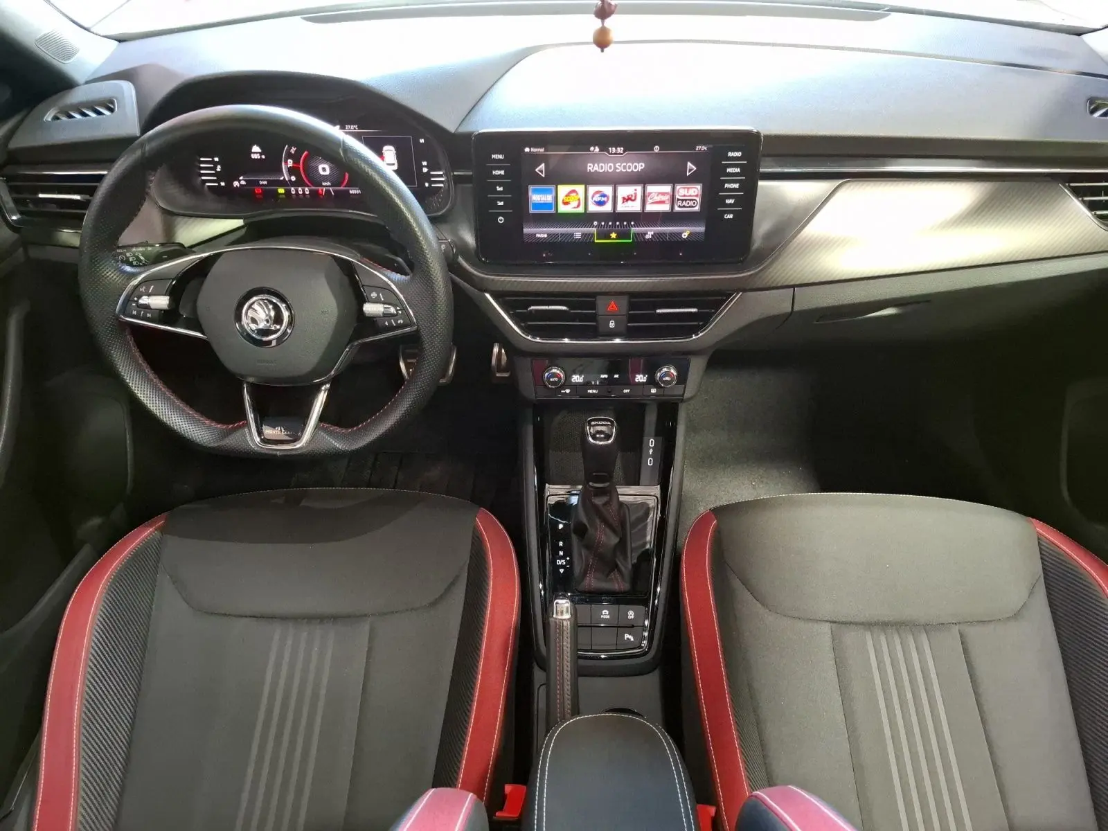 Vue intérieure frontale du Skoda Kamiq 1.0 TSI 110 Monte Carlo avec volant sport, écran tactile et sièges noirs à surpiqûres rouges.