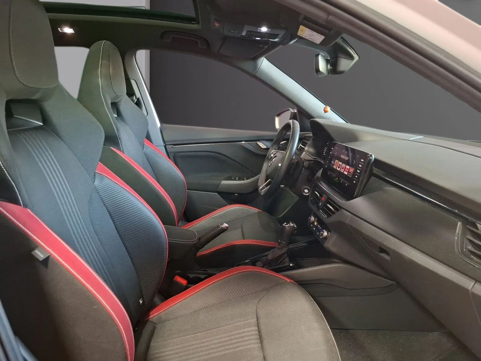 Vue intérieure côté conducteur du Skoda Kamiq 2021, sièges sport noirs avec surpiqûres rouges et tableau de bord moderne.