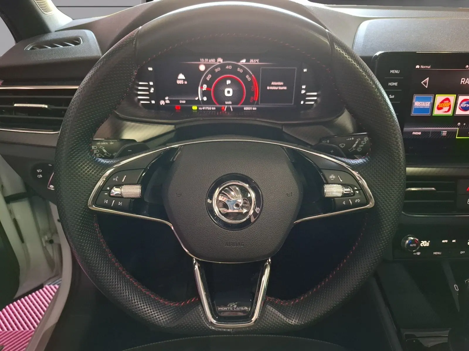 Vue centrée du volant noir perforé avec surpiqûres rouges d'une Skoda Kamiq Monte Carlo 2021, tableau de bord numérique allumé.