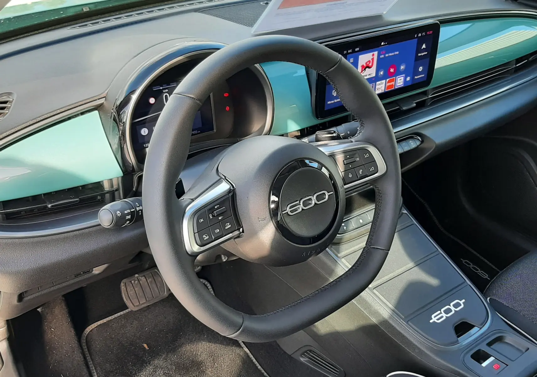 Vue intérieure de face du volant noir marqué 600, tableau de bord vert sky et écran tactile du Fiat 600 hybride 2025.