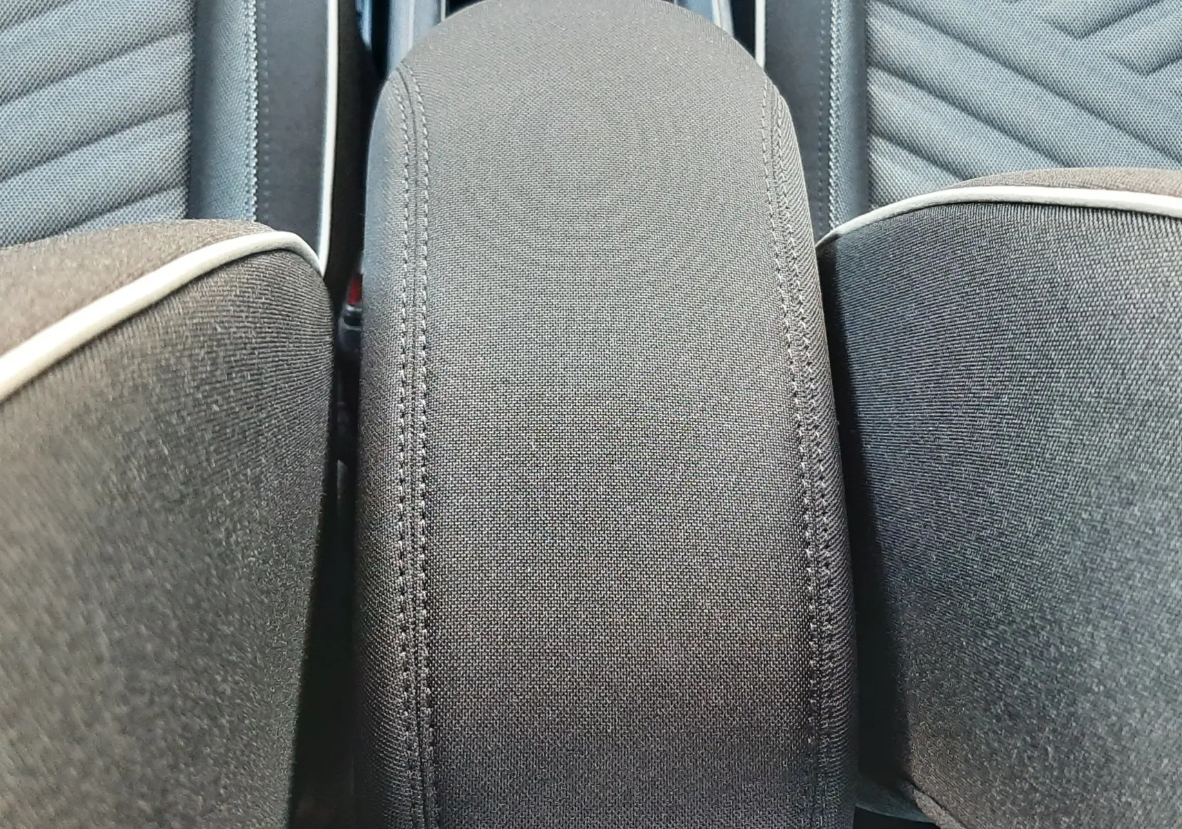 Détail de l'accoudoir central en tissu gris entre les sièges avant du Fiat 600 vert Sky 2025.