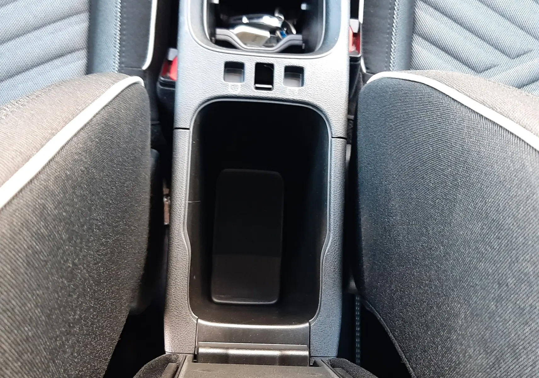 Gros plan sur la console centrale noire entre les sièges avant gris-beige du Fiat 600 1.2 Hybrid 2025.