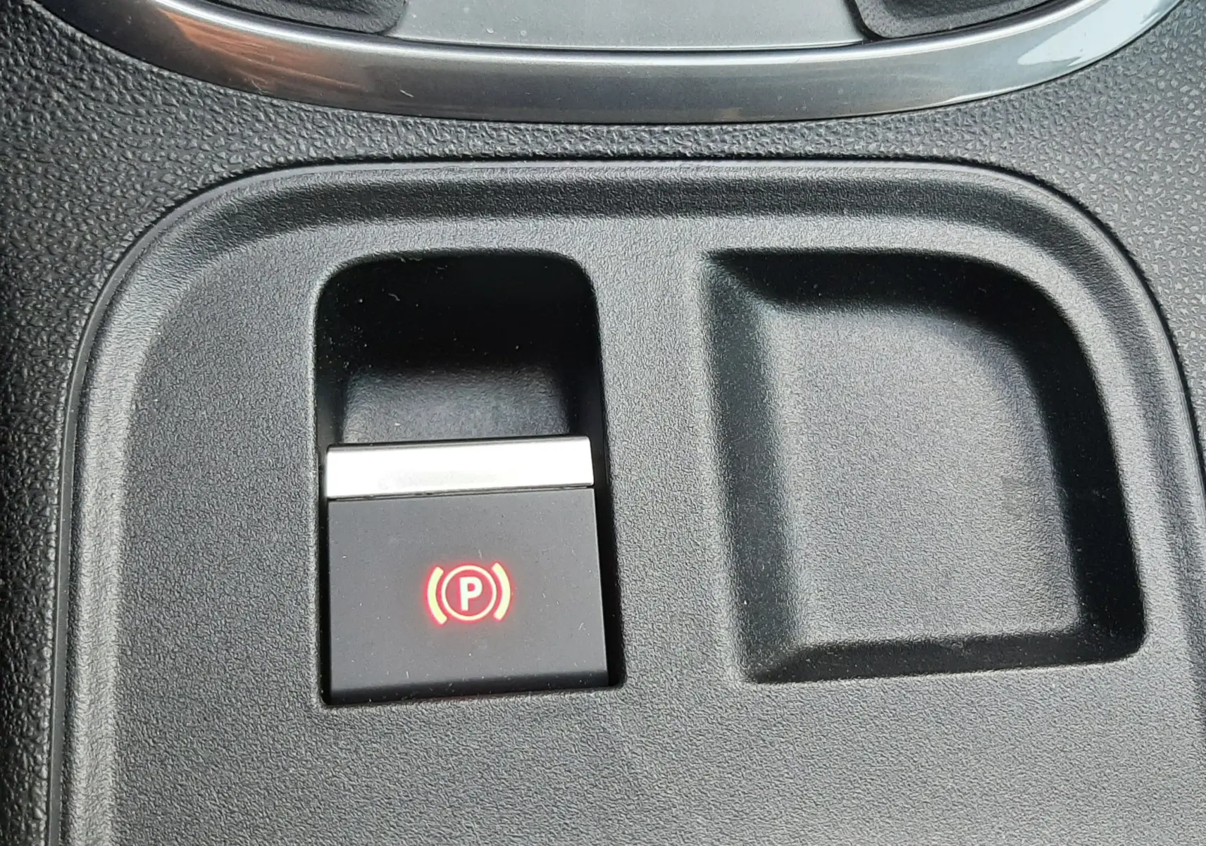 Gros plan sur le bouton de frein à main électronique rouge dans la console centrale d'une FIAT 600 1.2 Hybrid 2025 vert Sky.
