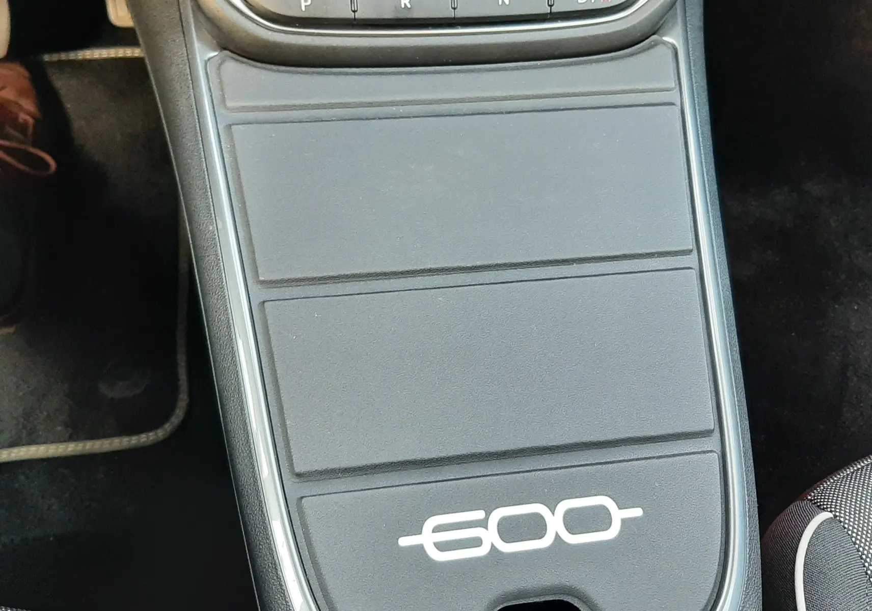 Vue plongeante sur la console centrale noire de la Fiat 600 1.2 Hybrid 2025 avec sélecteur de boîte auto et logo 600 blanc.