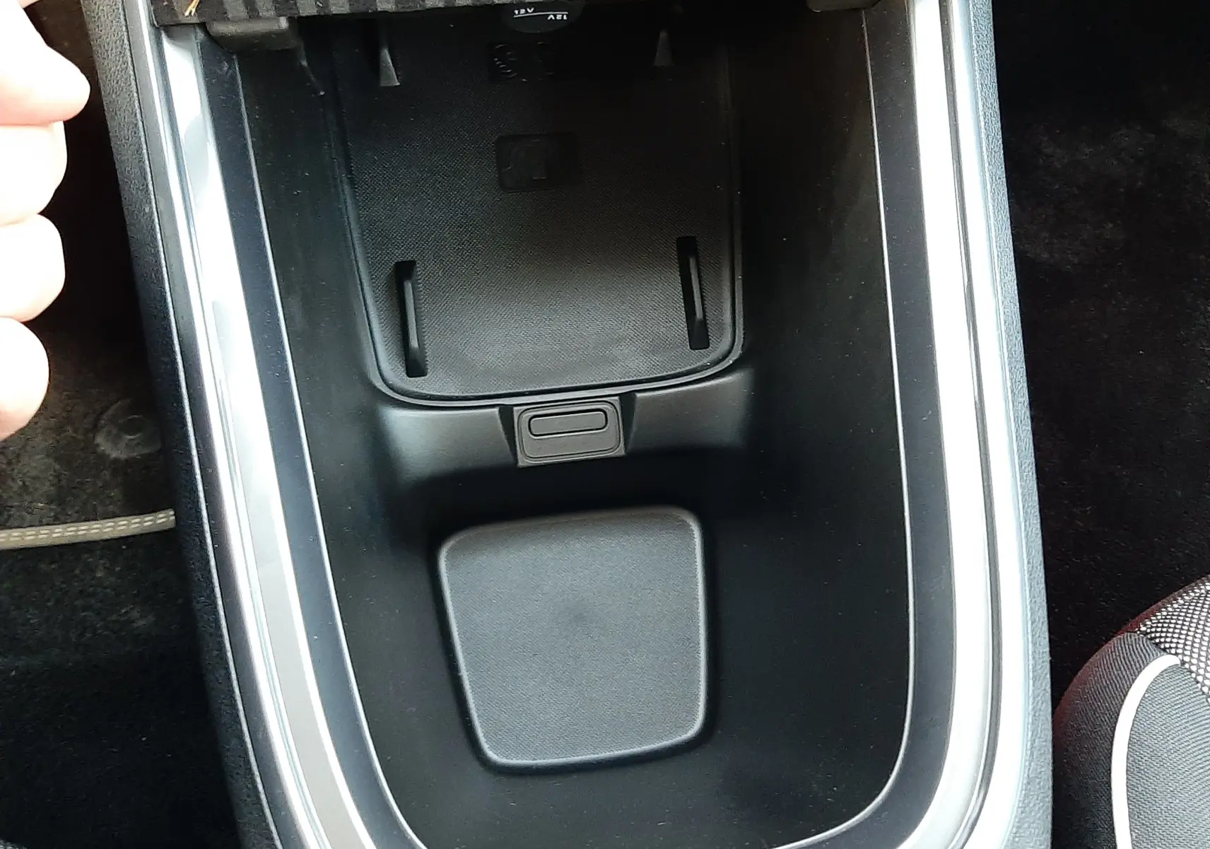 Vue rapprochée de la console centrale noire avec un compartiment de rangement et un cache FIAT dans une Fiat 600 hybride 2025.