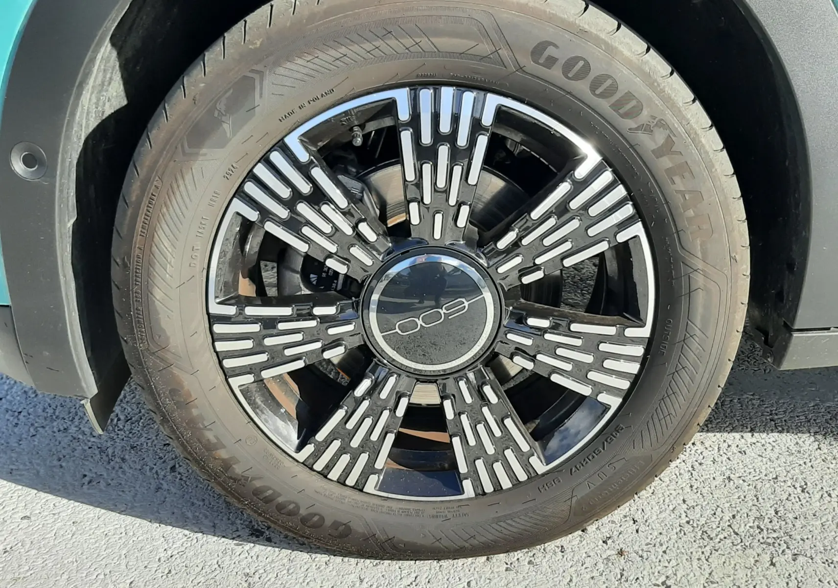 Gros plan sur la roue avant droite d'une FIAT 600 vert sky avec jante noire et motifs argentés distinctifs.