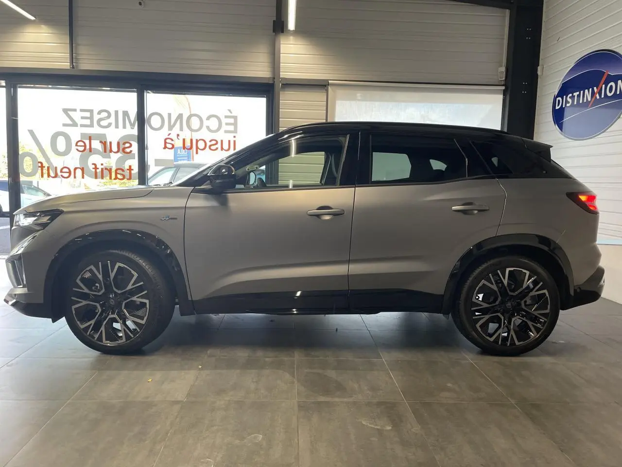 Profil côté gauche du Renault Austral gris satin mat avec toit noir et jantes alliage 20 pouces en intérieur showroom.