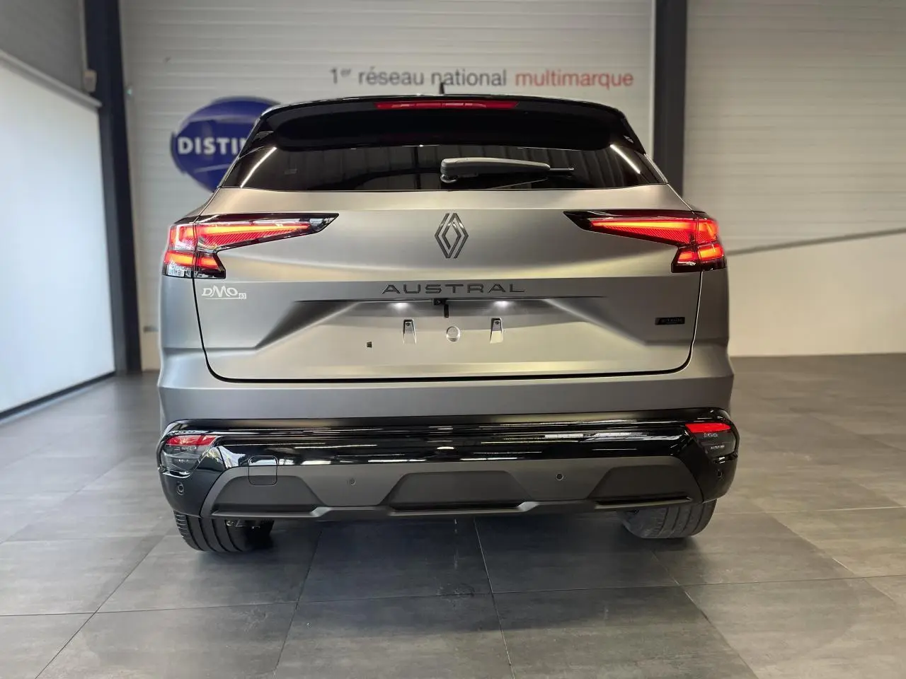 Vue arrière du Renault Austral 2025 gris satin mat avec toit noir et feux LED allumés en intérieur showroom.