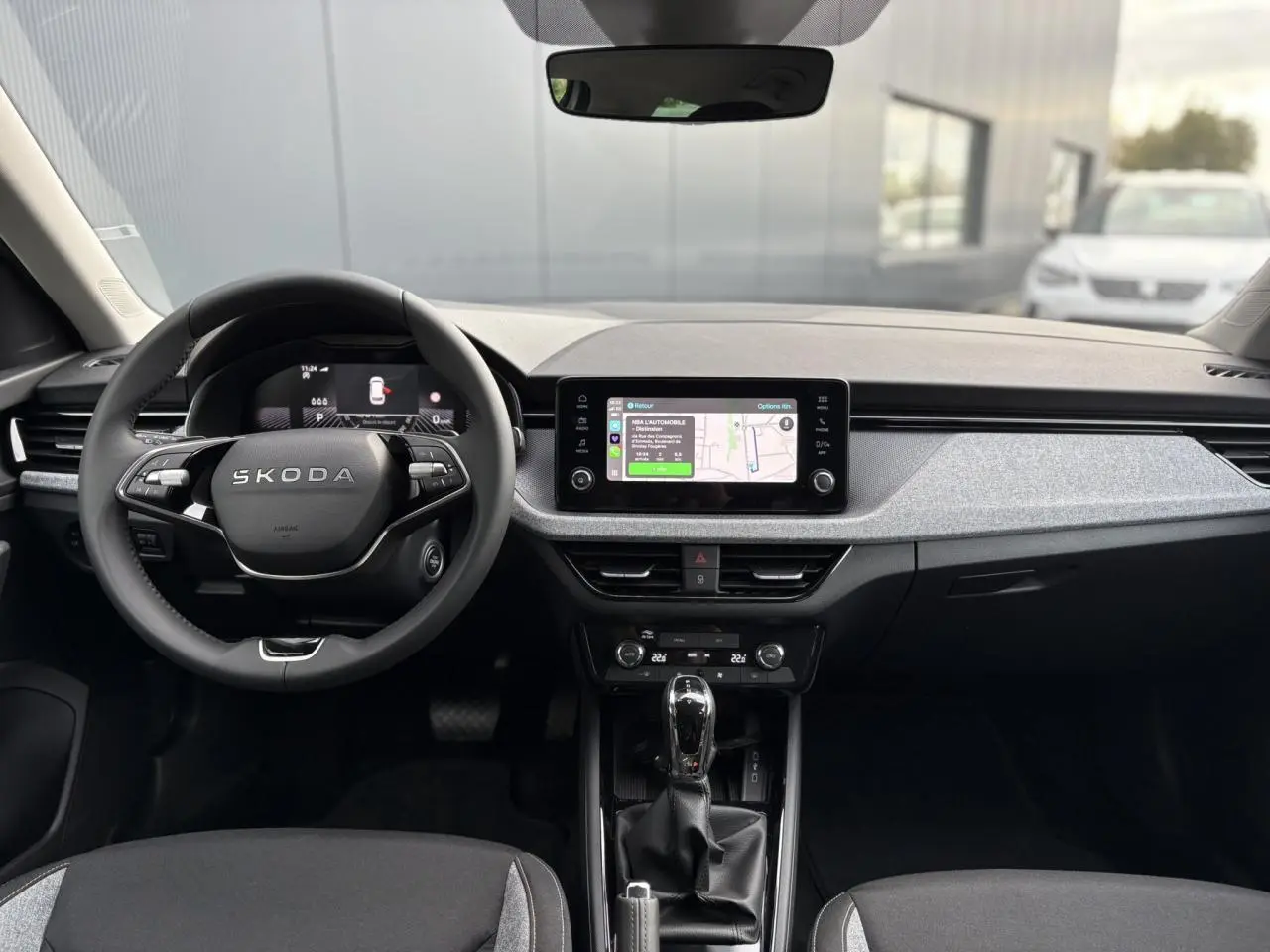 Vue intérieure frontale du Skoda Kamiq 2025, tableau de bord gris clair avec écran tactile et volant multifonctions noir.