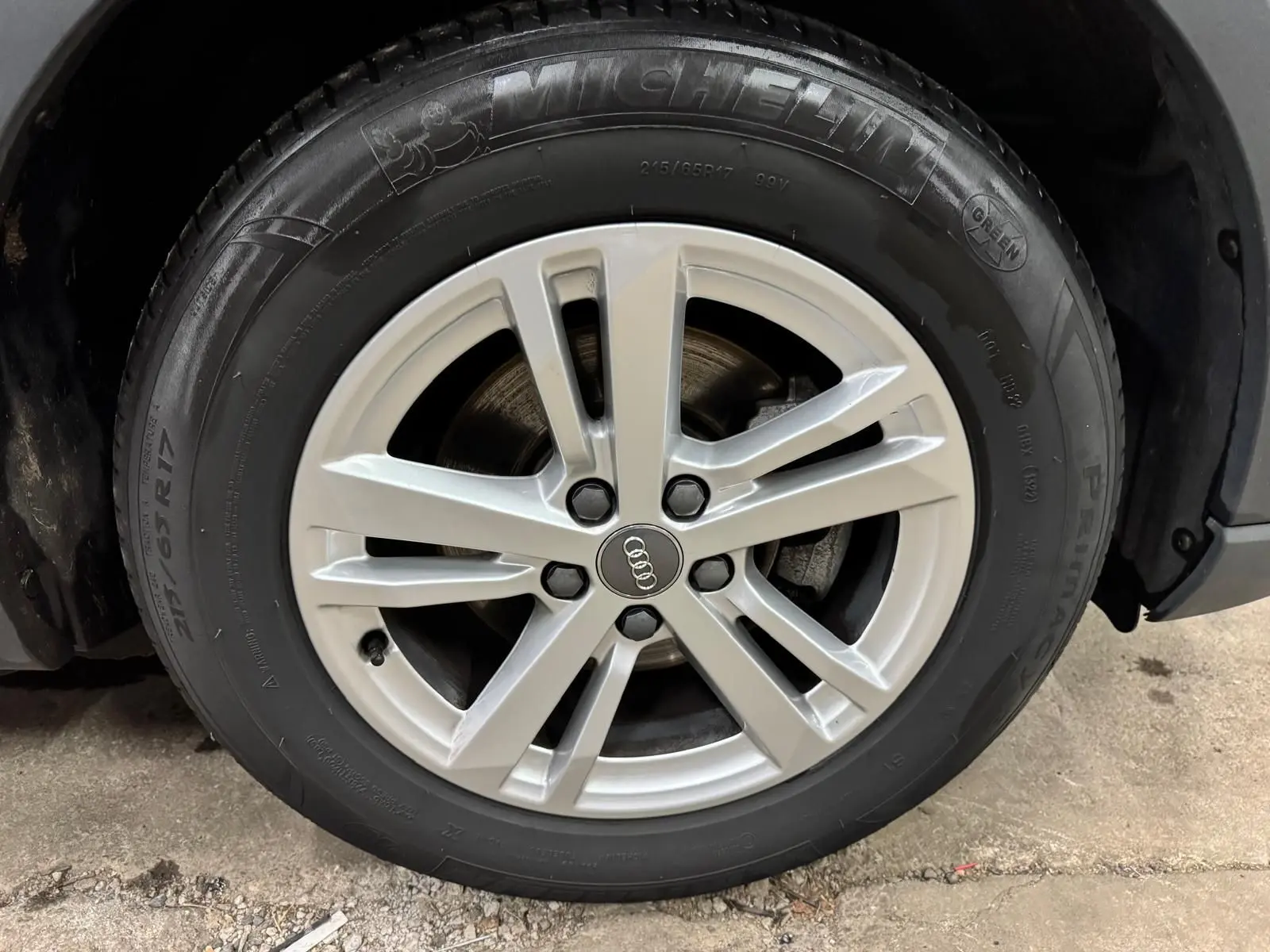 Gros plan sur la jante alliage argentée avec logo Audi d’un Audi Q3 Business gris, pneu Michelin visible.