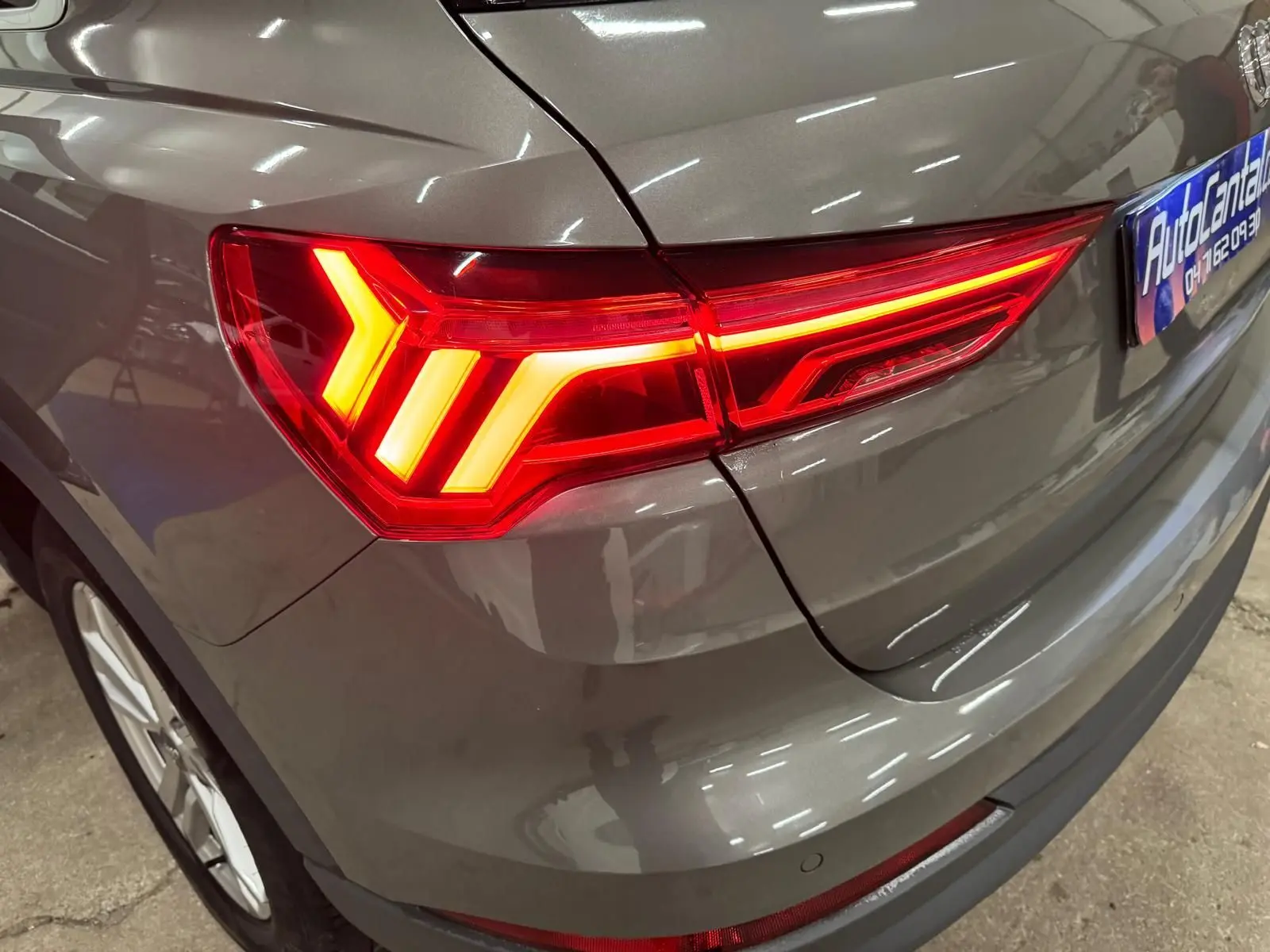 Gros plan sur le feu arrière droit allumé d'un Audi Q3 Business gris, avec partie de la roue et du pare-chocs visibles.