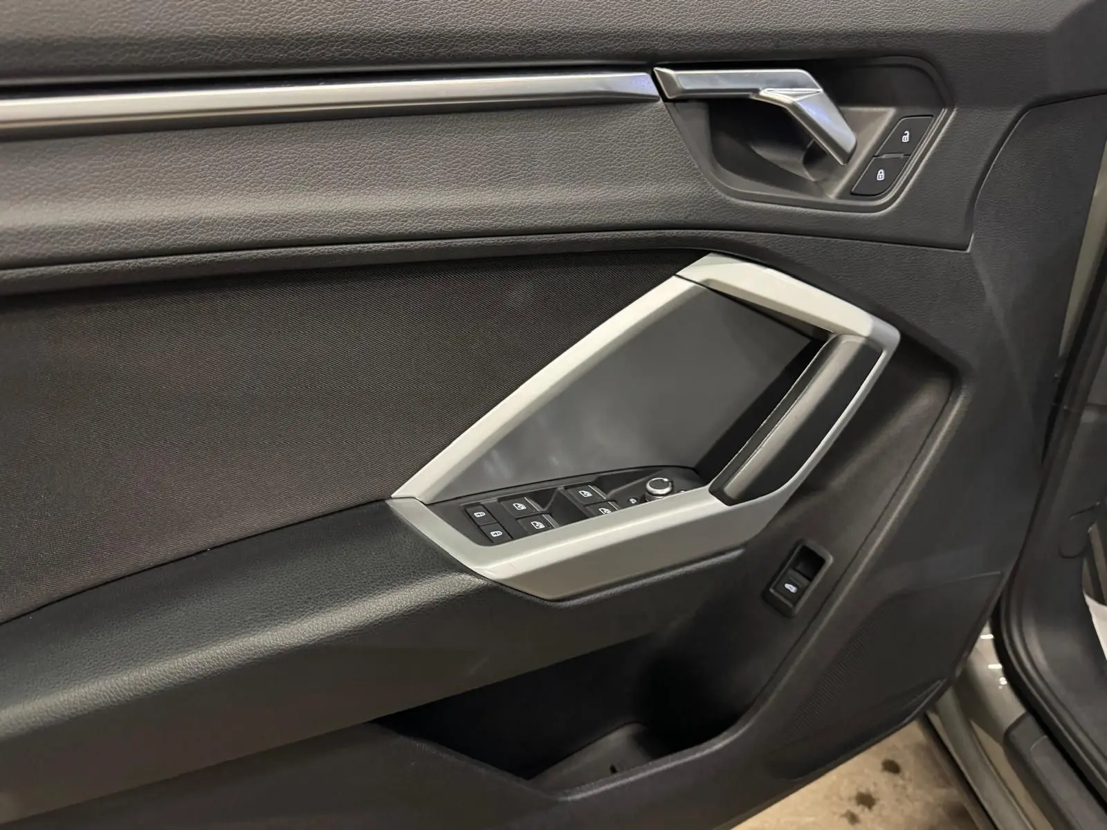 Gros plan sur la porte avant gauche de l'Audi Q3 Business gris, avec commandes de vitres et inserts noir brillant.