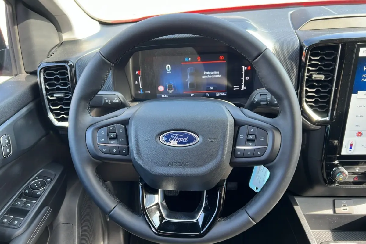 Vue rapprochée du volant cuir multifonctions noir du Ford Ranger 2025 avec tableau de bord numérique et commandes intégrées.
