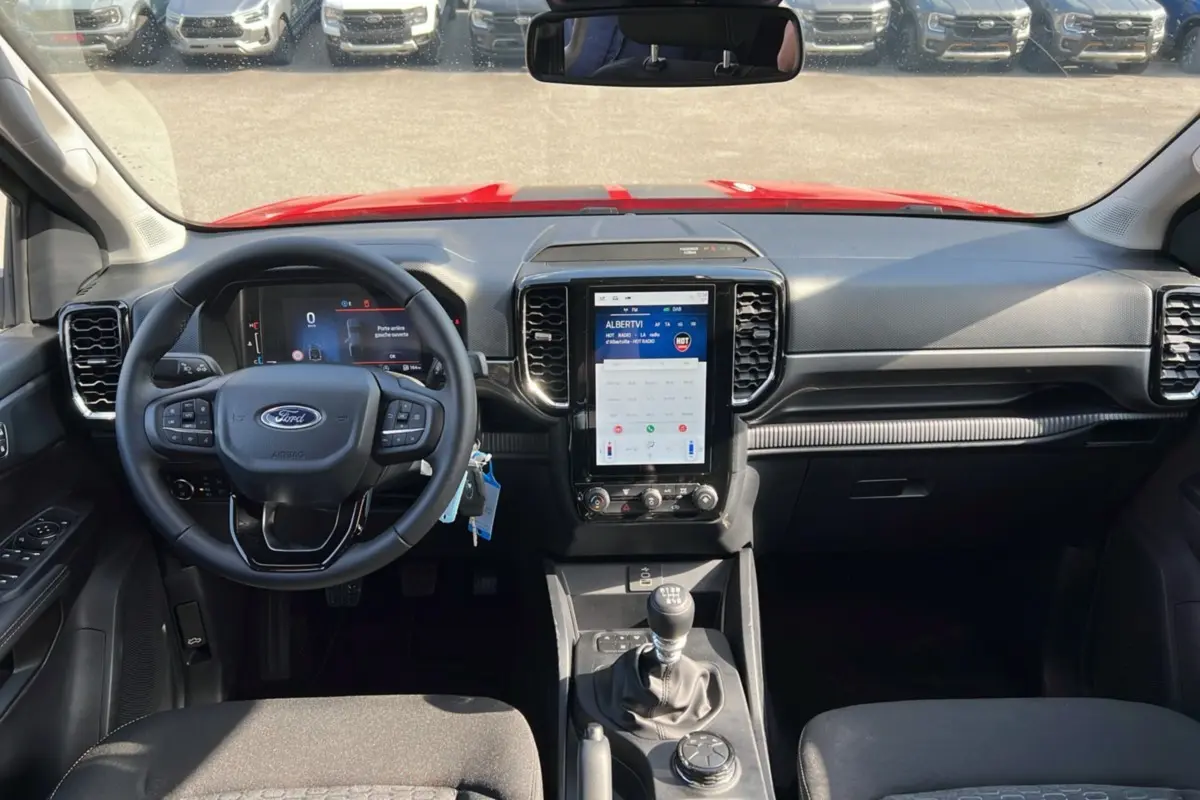 Vue intérieure avant du Ford Ranger rouge racing 2025, volant multifonctions, écran tactile vertical et boîte manuelle.