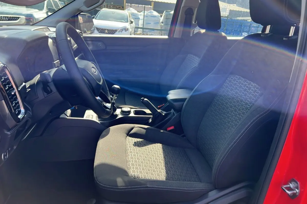 Vue intérieure côté conducteur du Ford Ranger rouge racing 2025, montrant sièges, volant cuir et levier de vitesse manuel.
