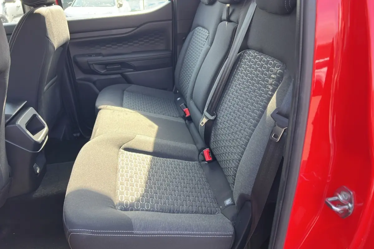 Vue latérale des sièges arrière noirs du Ford Ranger rouge racing 2025, avec ceinture de sécurité et porte ouverte.