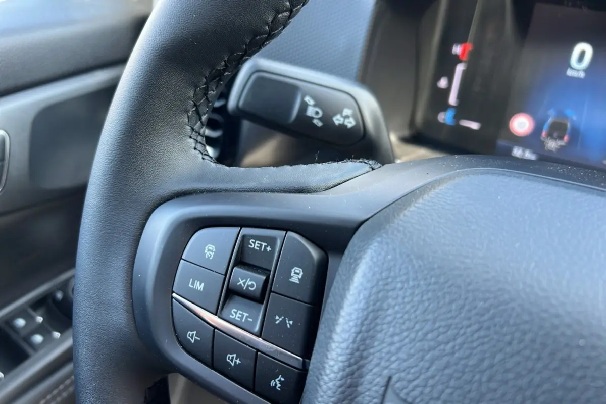 Gros plan sur le volant cuir multifonctions du Ford Ranger 2025, avec commandes de régulateur et tableau de bord numérique flou en arrière-plan.