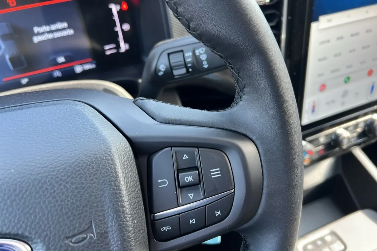 Gros plan sur le volant cuir multifonctions du Ford Ranger 2025 avec commandes intégrées et écran tactile en arrière-plan.