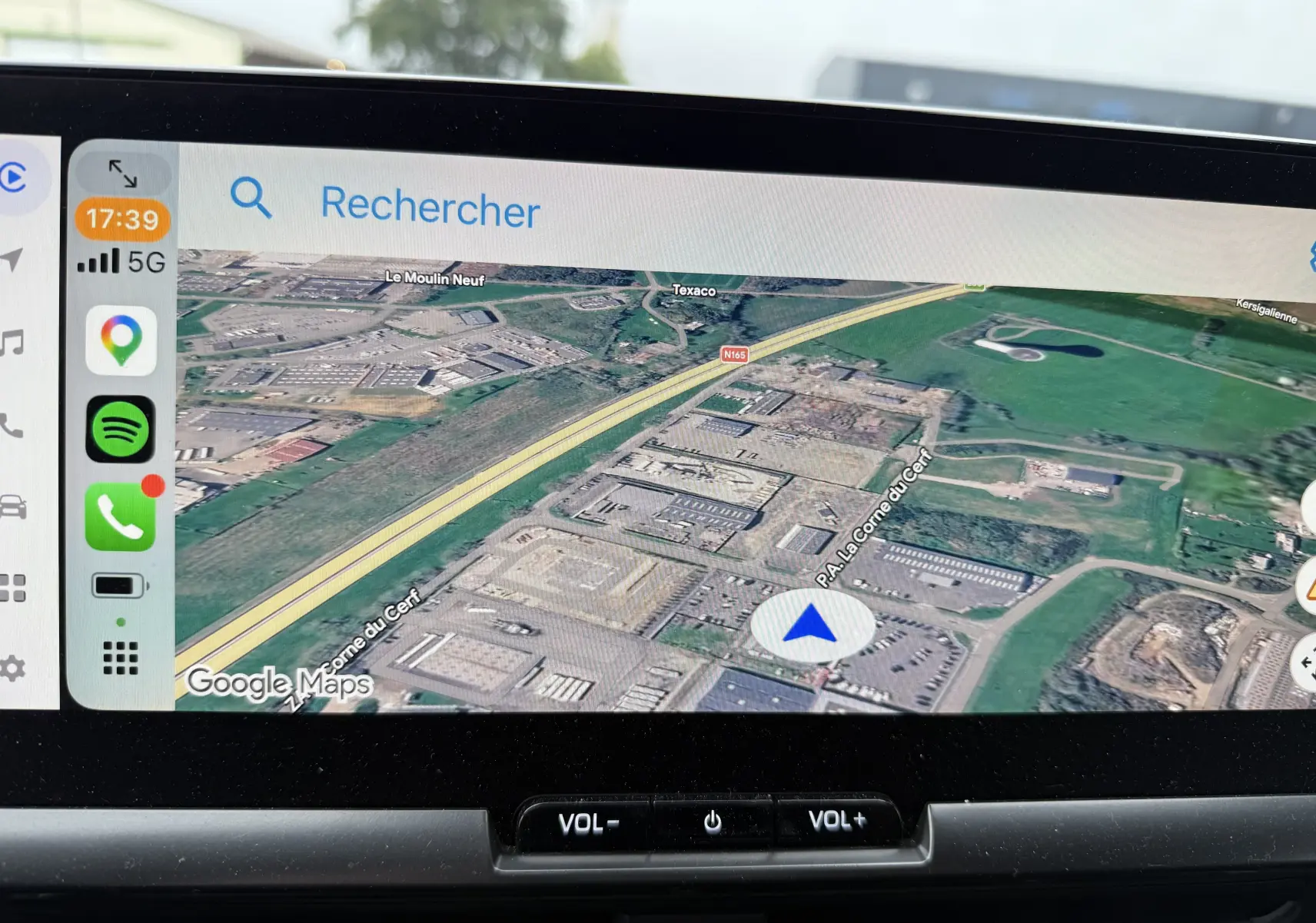 Écran tactile intérieur du Toyota C-HR hybride 2024 montrant la navigation GPS avec vue satellite et commandes volume en dessous.