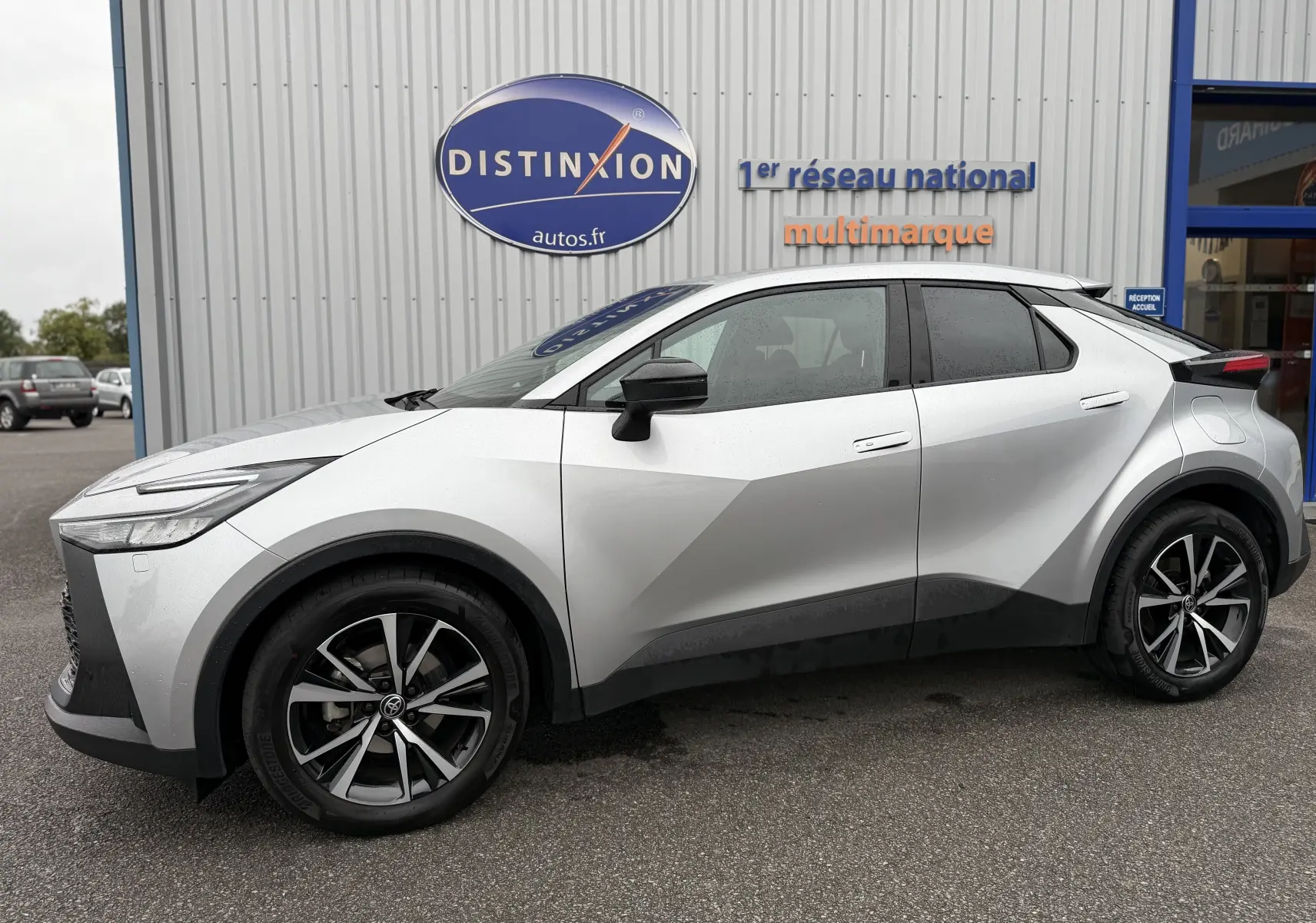 Vue de profil côté gauche du Toyota C-HR Hybride gris 2024 avec jantes bi-ton et lignes anguleuses marquées.