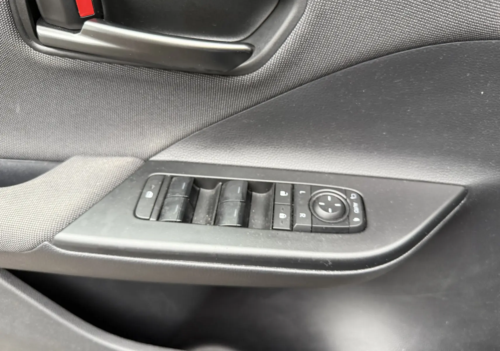 Gros plan sur la commande des vitres et le bouton de réglage des rétroviseurs côté conducteur du Toyota C-HR Hybride gris 2024.